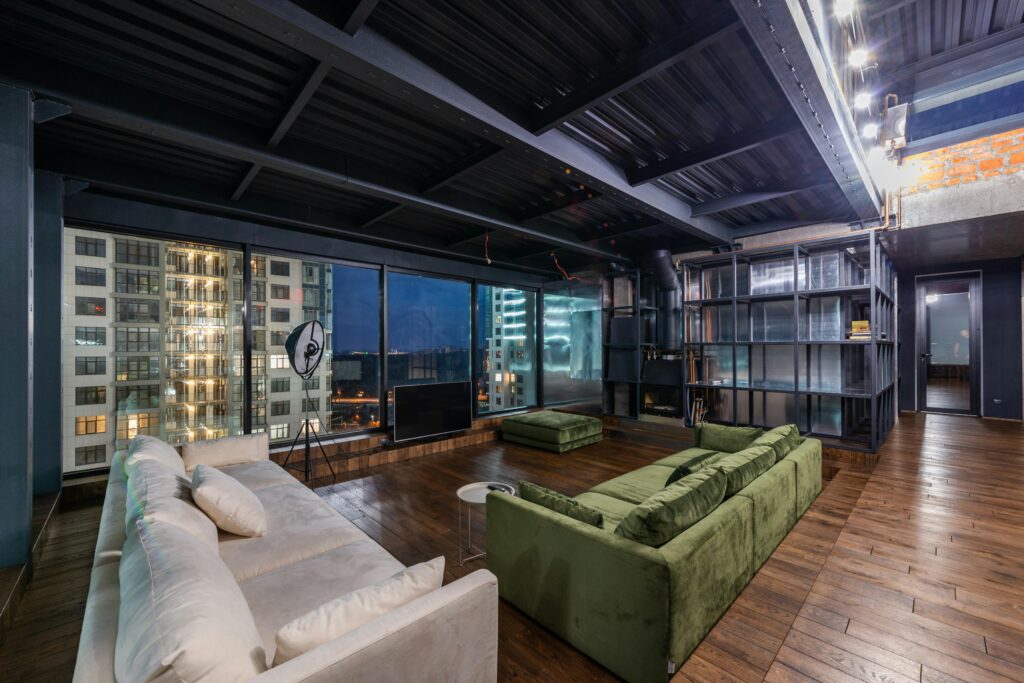 Interior of spacious modern living room with comfortable green and white sofas and panoramic windows in contemporary apartment in evening time